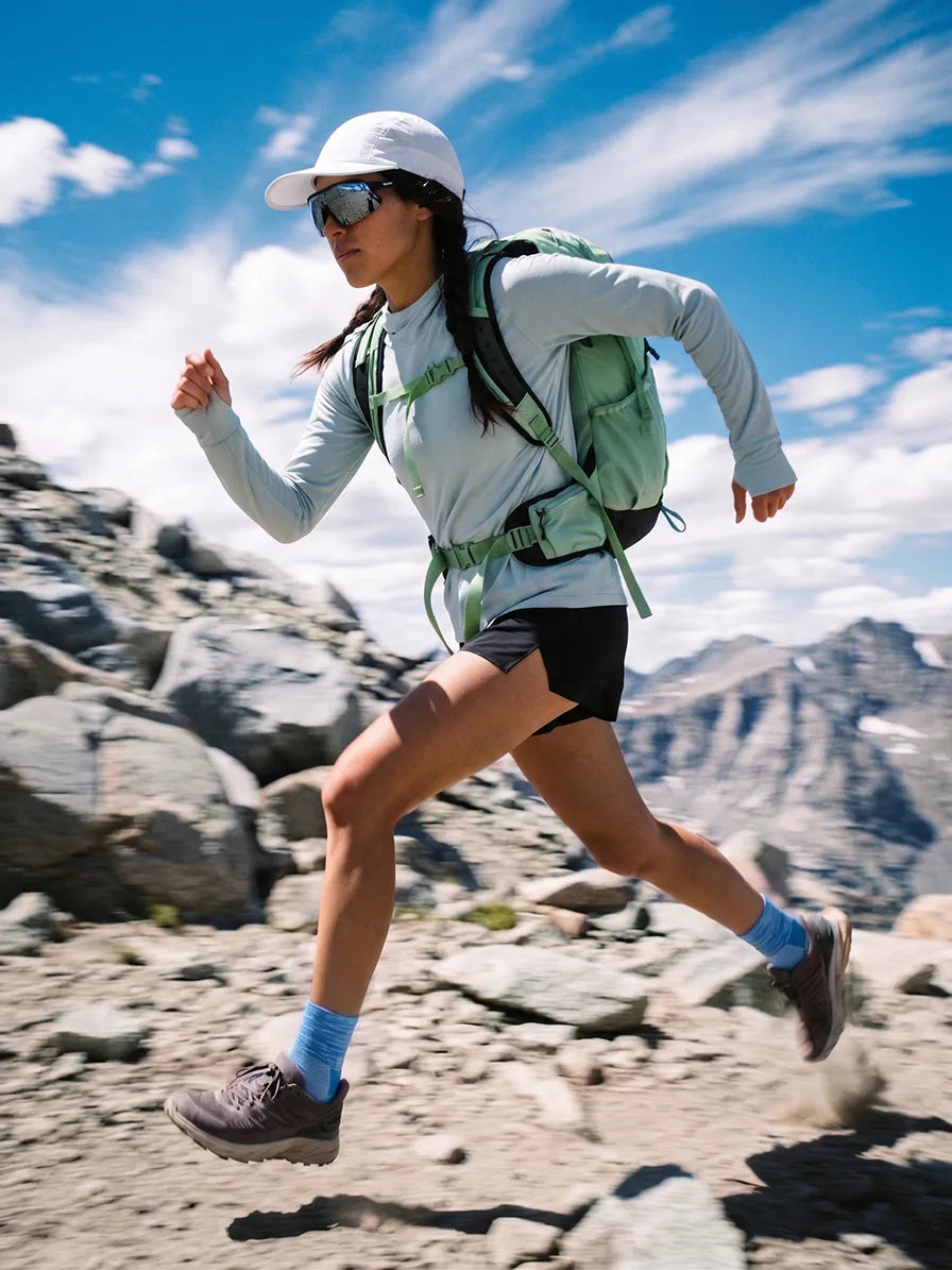 Female trail runner wearing blue socks and a backpack on a rocky mountain trail