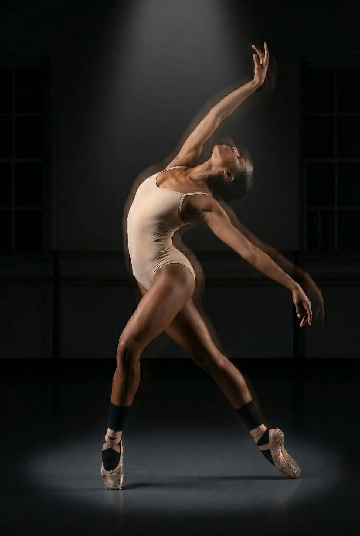 A ballet dancer performing a dynamic backbend pose under a spotlight, showcasing a beautiful motion blur effect with pink pointe shoes and black YG Socks in a dance studio.
