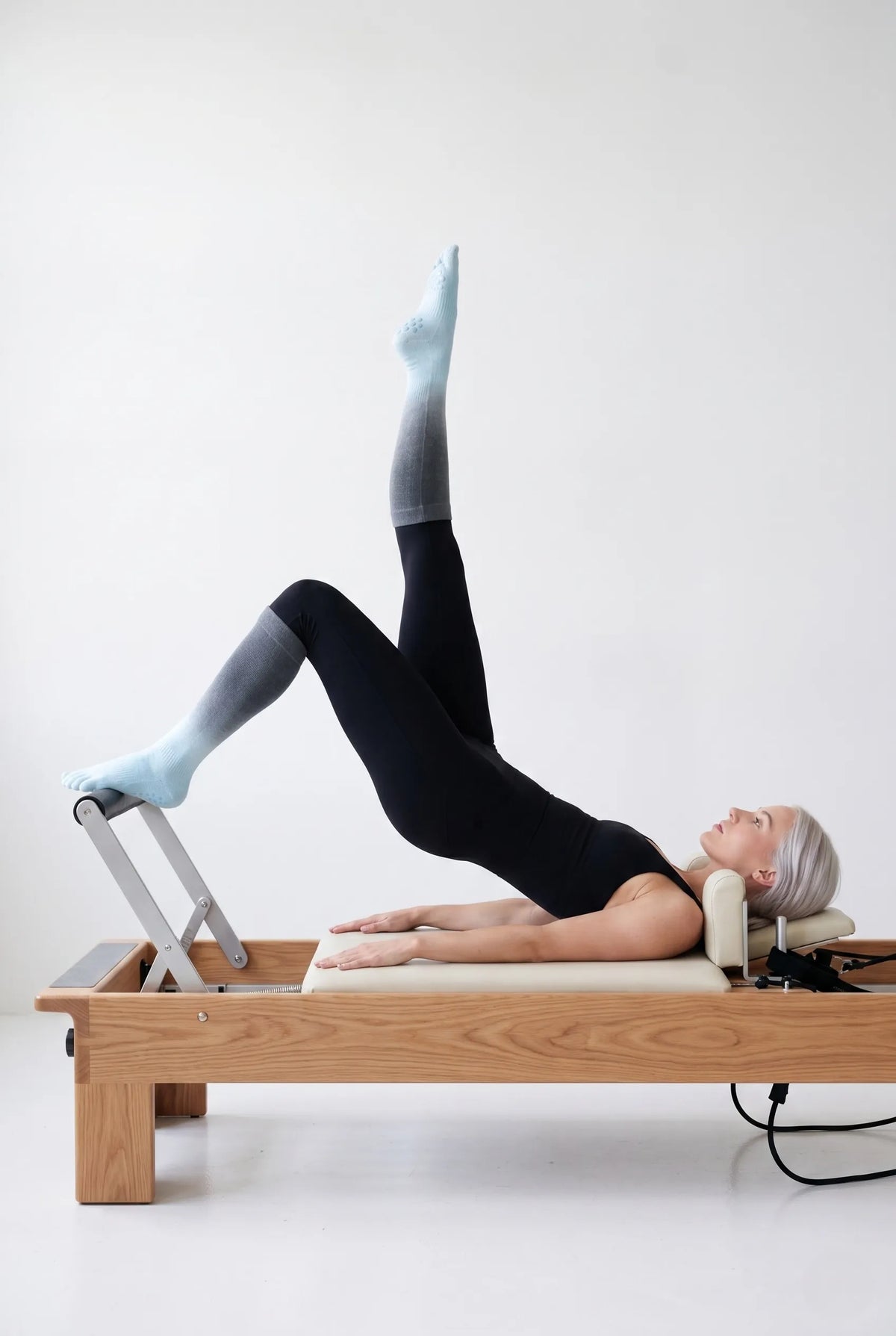Side view of a pilates practitioner lifting one leg in perfect alignment on a Reformer, showcasing YG Socks premium non-slip toe socks designed for advanced core training and fluid control.