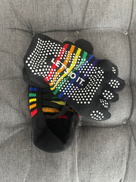 A real customer photo by Jennifer showcasing YG Socks black criss-cross grip socks, highlighting the vibrant rainbow stripes, white non-slip dots, and "LET'S DO IT" text on a grey textured cushion.