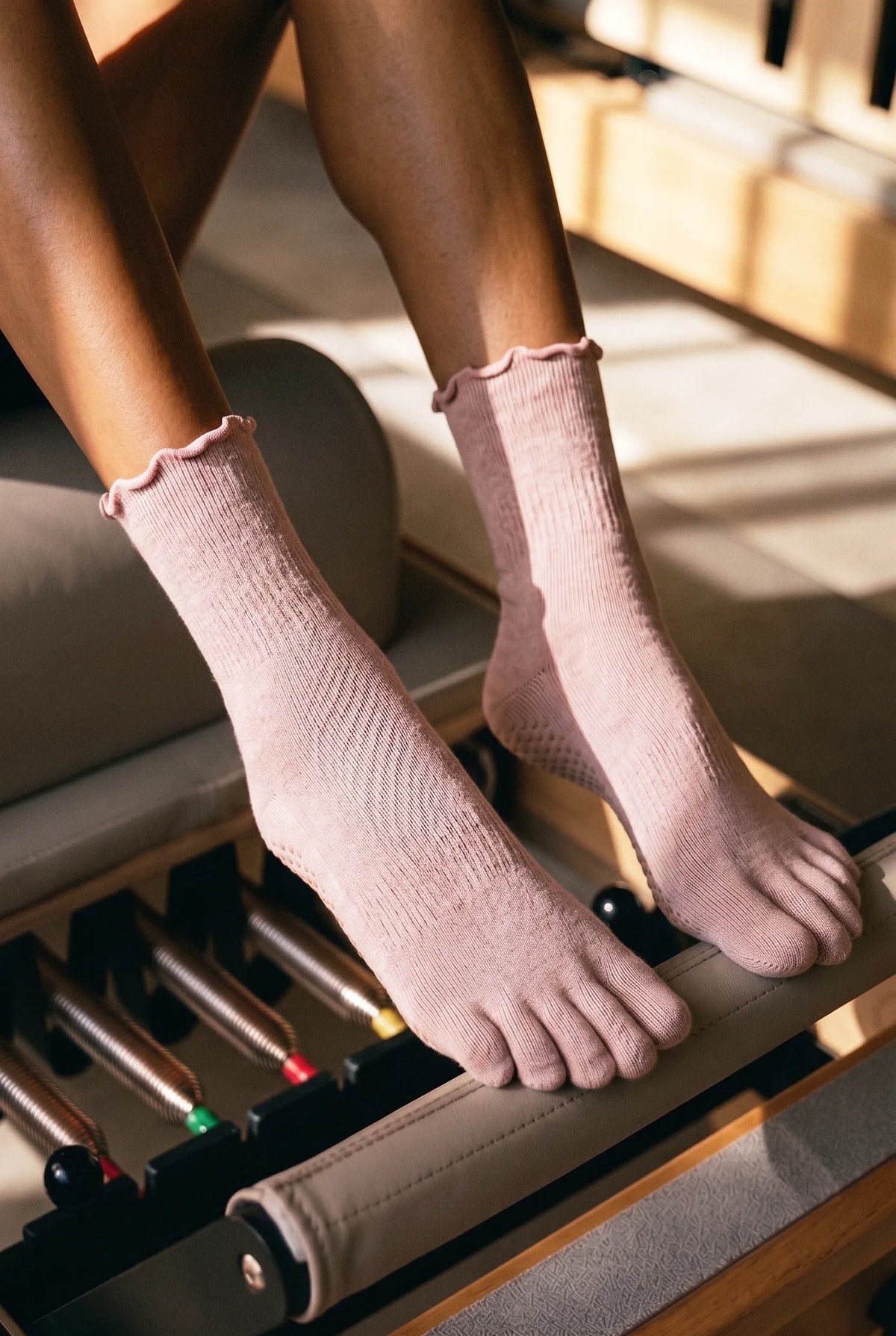 Shop Pilates Essentials collection of pink ribbed five-toe grip socks on a reformer.