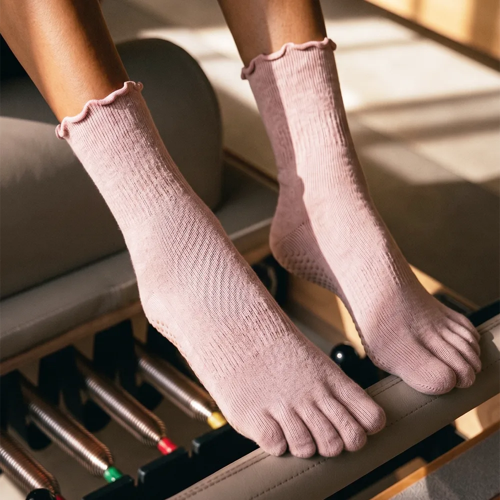Shop Pilates Essentials collection of pink ribbed five-toe grip socks on a reformer.