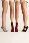 Three models wearing YG Socks premium non-slip five-toe grip socks designed for pilates, yoga, and barre, showcasing different styles including open-back and crew length on a minimalist clean background.